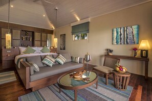 A modern living room with a sofa, a round coffee table, and a chair. There is a painting on the wall and a lamp on a side table. - Hurawalhi Island Resort Maldives (Huruvalhi)