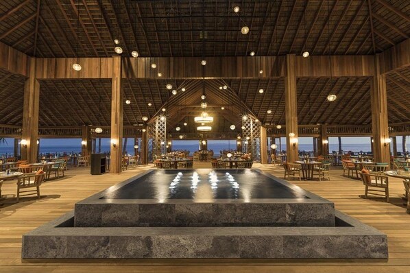 A spacious outdoor dining area with a central pool, wooden beams, and tables and chairs arranged around it. - Hurawalhi Island Resort Maldives (Huruvalhi)