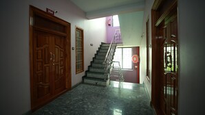 A hallway with a marble floor, wooden doors, and a staircase leading to a landing. - Royal Castle Residency (Puducherry)