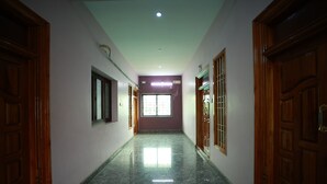 A hallway with wooden doors, a window with bars, and a tiled floor. - Royal Castle Residency (Puducherry)