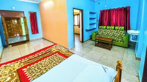 A room with a bed, a green sofa, a red curtain, and a ceiling fan. - Royal Castle Residency (Puducherry)
