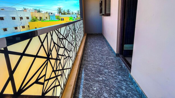 A balcony with a geometric railing, a view of neighboring buildings, and a door leading to an interior space. - Royal Castle Residency (Puducherry)