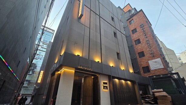 A modern hotel with a prominent 'Nesto' sign, large windows, and a brick building in the background. - Nesto Hongdae (Seoul)