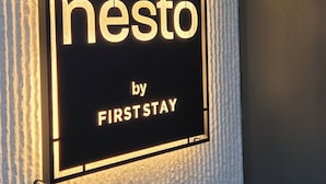 A sign with the text "nesto by FIRSTSTAY" mounted on a textured wall. - Nesto Hongdae (Seoul)