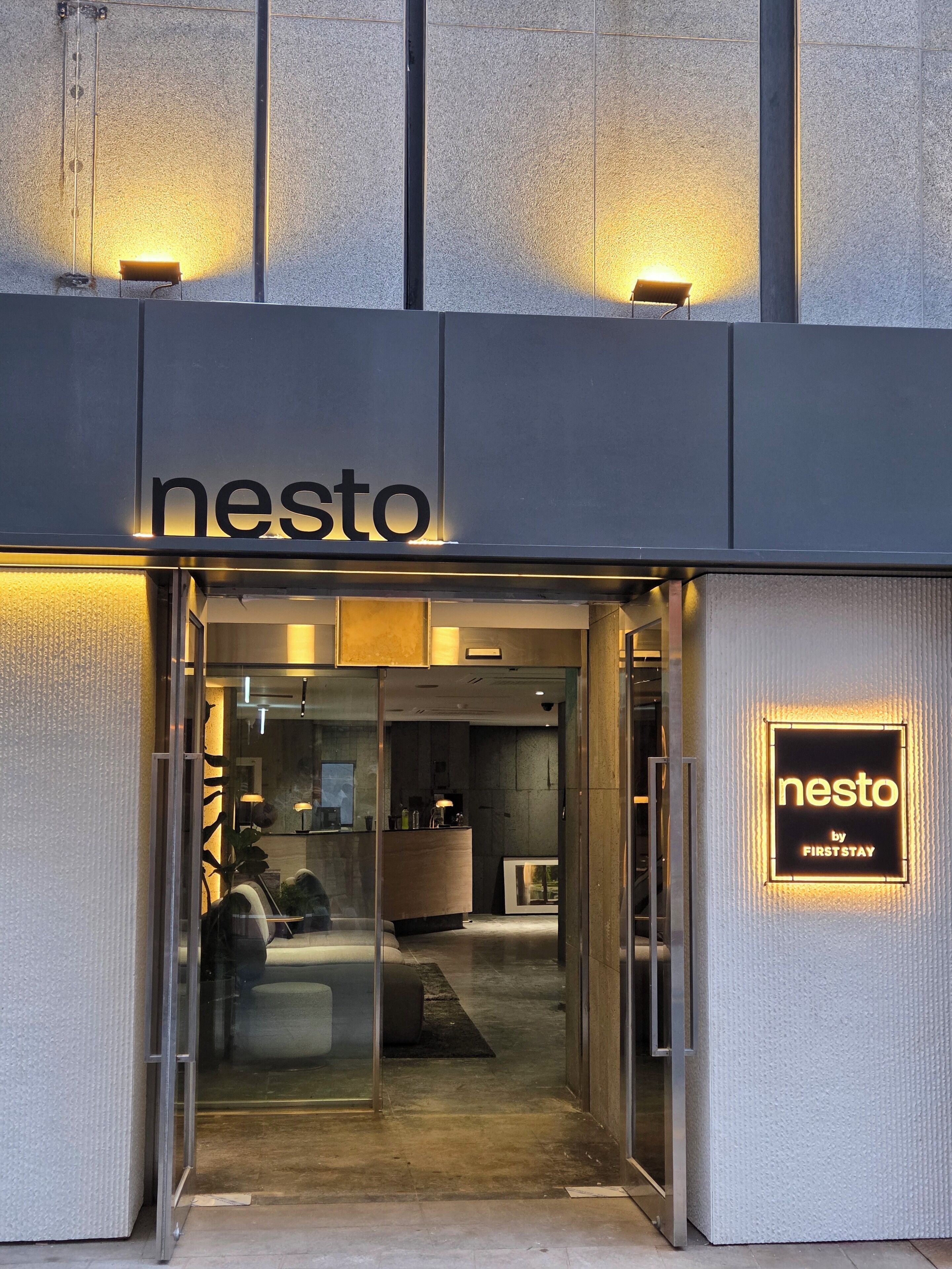 The entrance to a hotel named 'nesto' with a modern design, featuring a reception desk and a glass door.