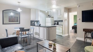 Een moderne keuken met witte kasten, een zwart aanrecht en een eethoek met een tafel en stoelen.