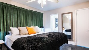 Een slaapkamer met een groot bed, groene gordijnen, een plafondventilator en een deur naar een andere kamer.
