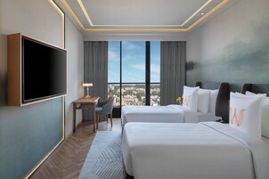 Habitación de hotel con dos camas, televisión de pantalla plana, escritorio y un ventanal con vistas a la ciudad.