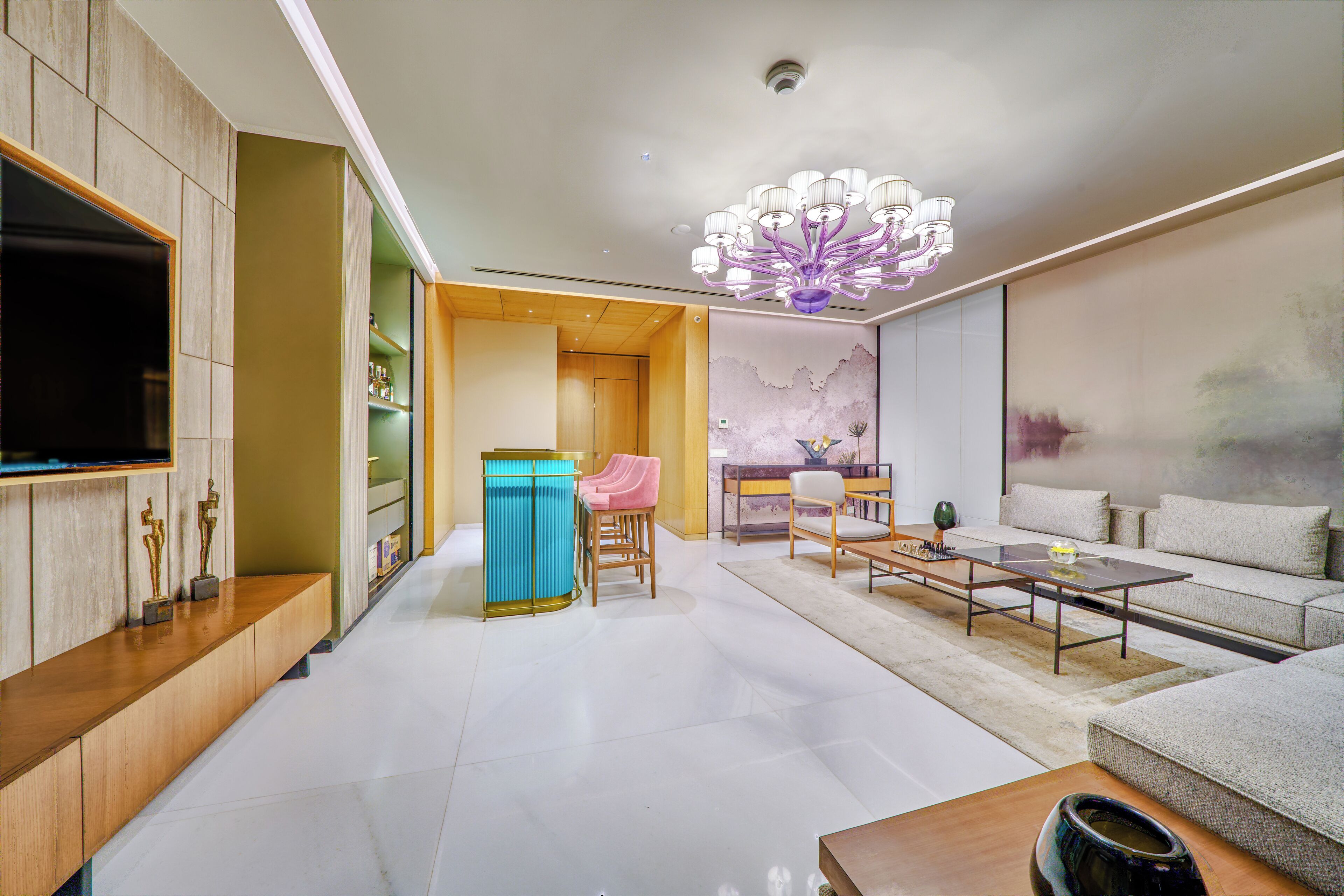 A modern living room with a large flat-screen TV, a chandelier, a sofa, and a coffee table.