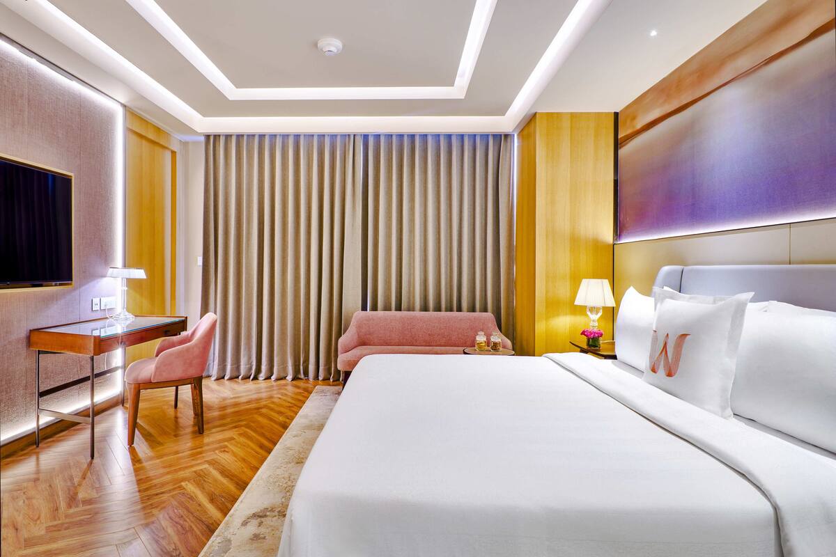 Une chambre d’hôtel avec un grand lit, un bureau avec une chaise, une télévision et un rideau.