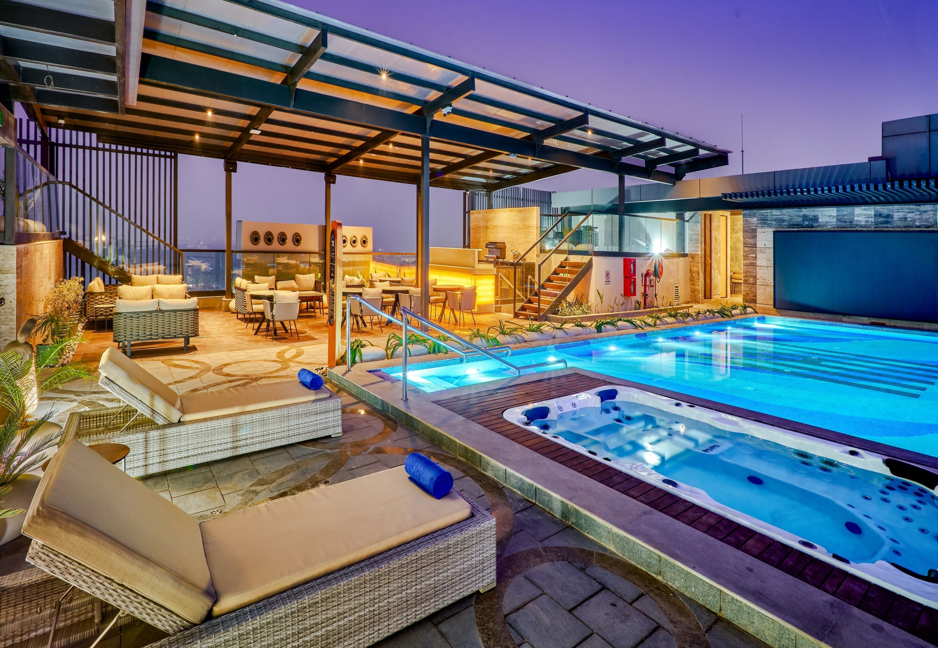 A rooftop pool area with lounge chairs, a hot tub, and a covered seating area.