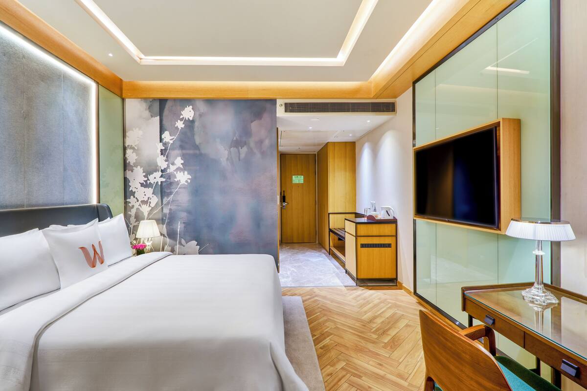 Une chambre d’hôtel avec un lit, un bureau, une télévision et un mur décoré de motifs floraux.