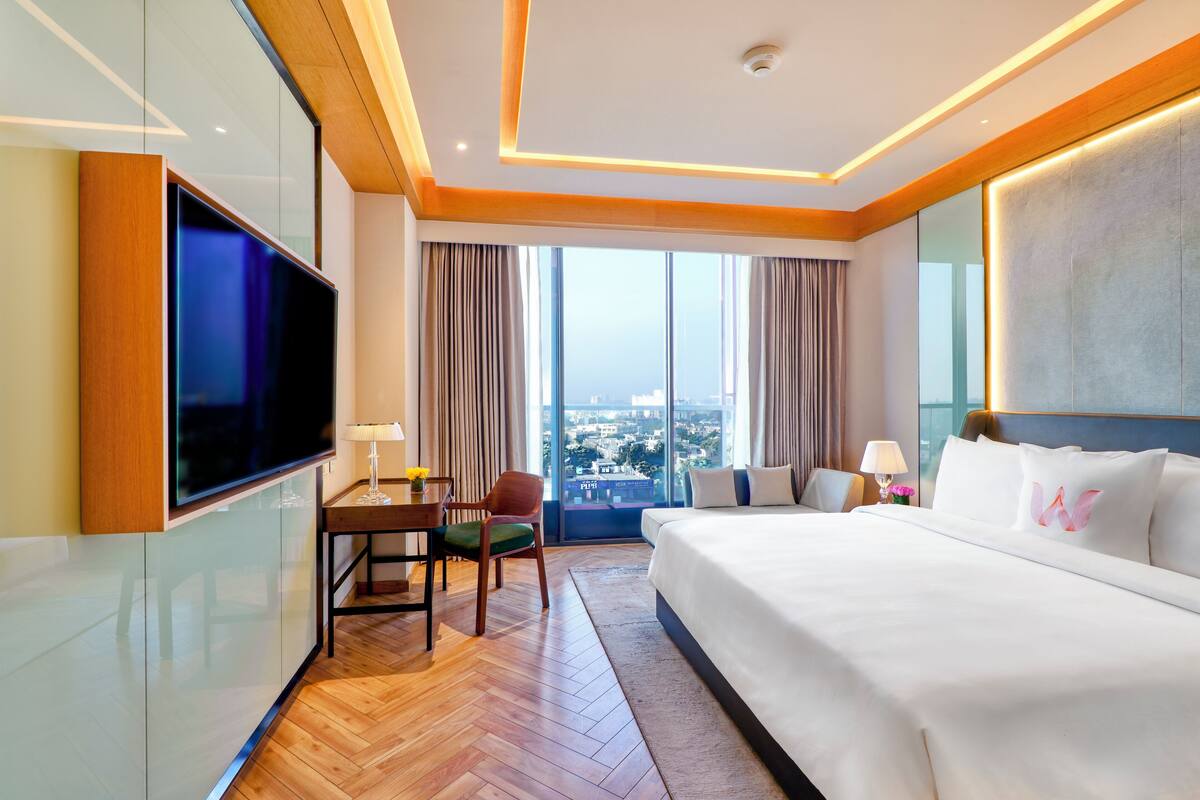 Une chambre d’hôtel dotée d’un grand lit, d’un téléviseur à écran plat, d’un bureau avec une chaise et offrant une vue sur la ville grâce à de grandes fenêtres.