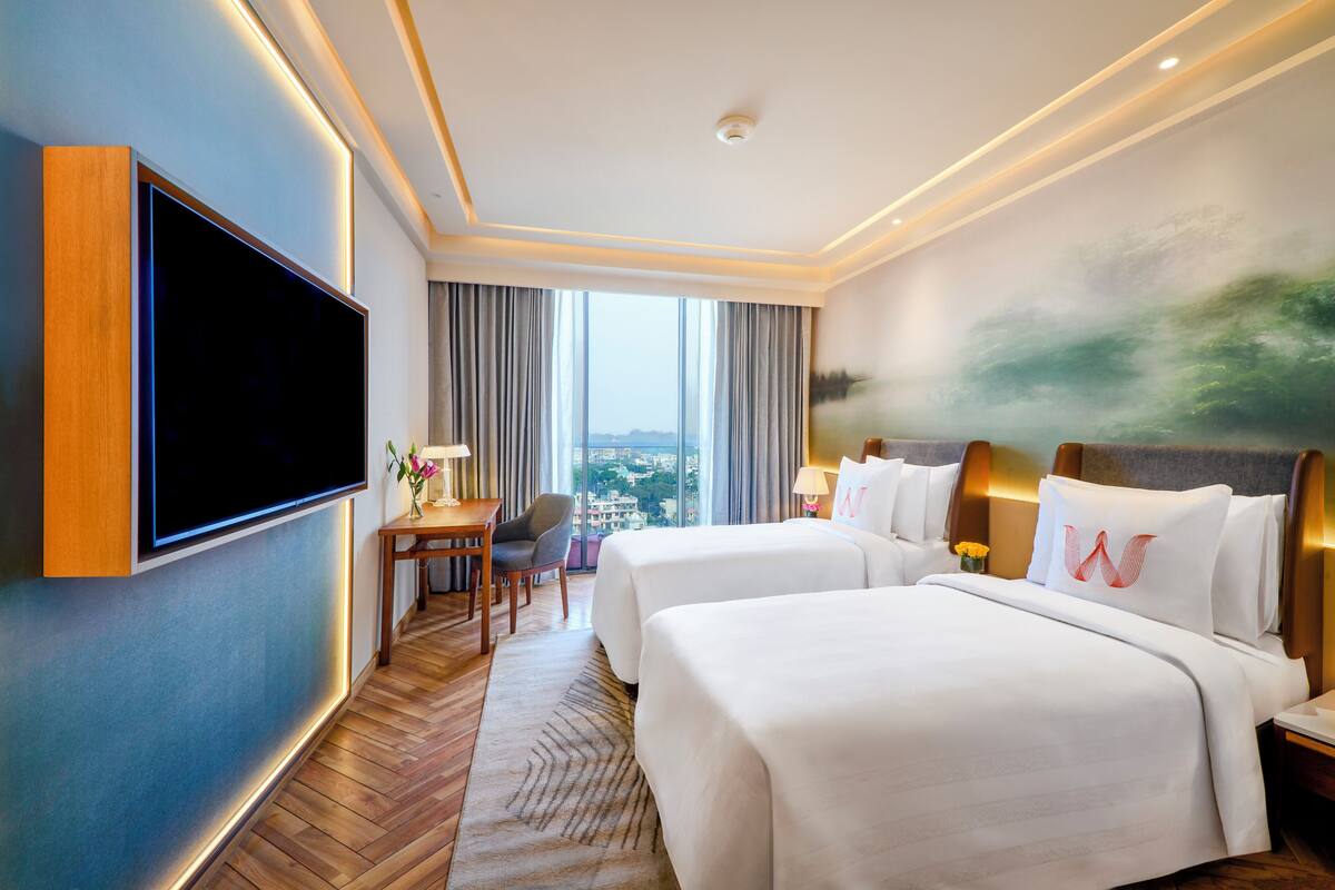 Une chambre d’hôtel équipée d’une télévision à écran plat, de deux lits, d’un bureau et offrant une vue sur la ville.