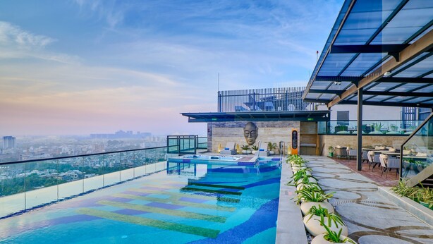 Piscina infinita en la azotea con vistas a la ciudad, una estatua y mobiliario exterior.