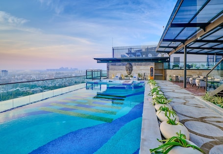 Piscina infinita en la azotea con vistas a la ciudad, una estatua y mobiliario exterior.