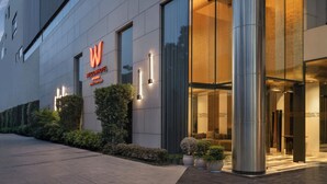 Una entrada de hotel moderna con un gran letrero con la letra 'W', exterior bien iluminado y plantas en macetas.