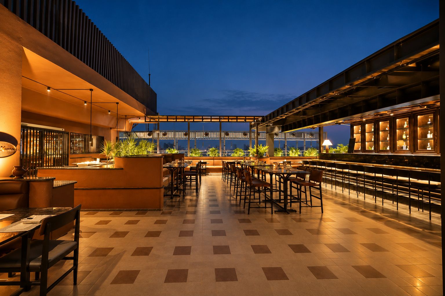 A rooftop bar with a checkered floor, seating arrangements, and a view of the cityscape at dusk.