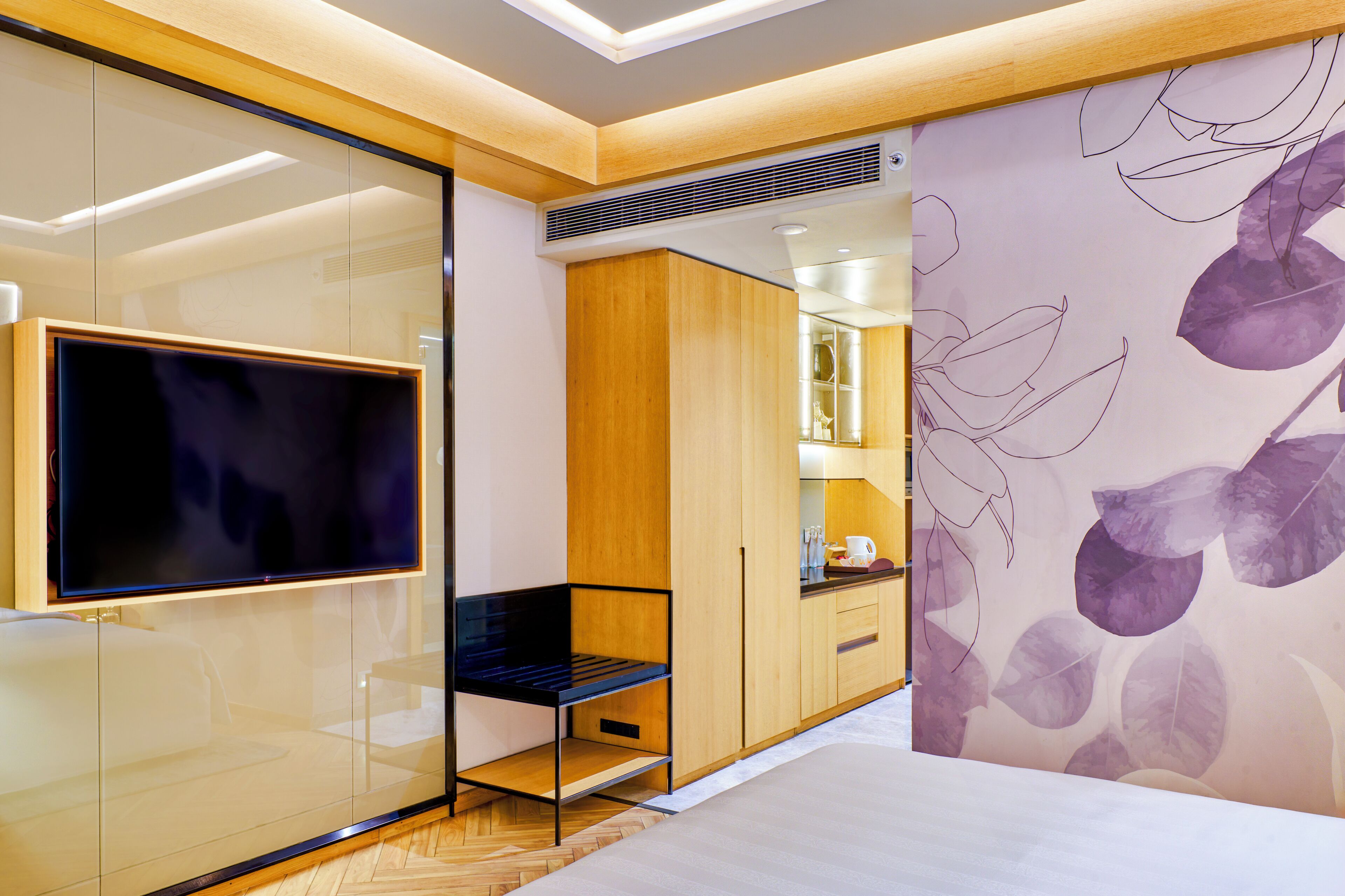 Un dormitorio moderno con televisor, armario de madera y pared con diseño de hojas.