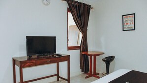 Una habitación con una cama, un televisor sobre una mesa de madera, una pequeña mesa redonda, una silla, una ventana con cortinas y un cartel motivacional en la pared.