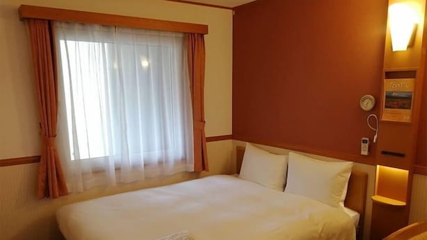 A hotel room with a large bed, a window with curtains, a bedside table with a lamp, and a wall clock. - Toyoko Inn Tokyo Yamanote-sen Otsuka-eki Kita-guchi No.2 (Tokyo)