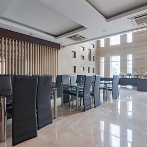 A modern dining area with black chairs and a glass table, large windows, and a wooden panel wall. - Urbanview Hotel Newton Riau Bandung (Bandung)
