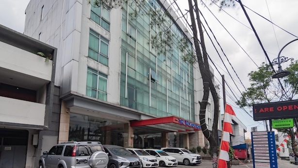 A hotel with a modern facade, multiple parking spaces, and a sign indicating the availability of various amenities. - Urbanview Hotel Newton Riau Bandung (Bandung)