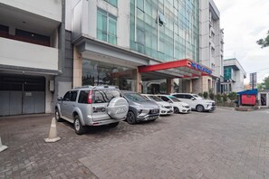 A hotel with a modern design, featuring a red awning and a glass facade. Several cars are parked in front, and a traffic cone is visible on the ground. - Urbanview Hotel Newton Riau Bandung (Bandung)