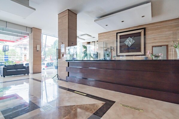 A modern reception area with a marble floor, a reception desk, and a large window offering a view of the street. - Urbanview Hotel Newton Riau Bandung (Bandung)