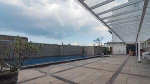 A rooftop pool area with a glass enclosure, a concrete wall, and a potted plant. - Urbanview Hotel Newton Riau Bandung (Bandung)