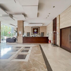 A hotel reception area with a marble floor, a reception desk, and a large wooden door. - Urbanview Hotel Newton Riau Bandung (Bandung)