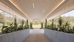 Un pasillo cubierto con techo de listones de madera y vistas a un jardín ajardinado.