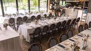Un restaurante con varias mesas dispuestas para comensales, asientos exteriores con sombrillas y vistas al jardín.
