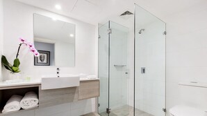 A modern bathroom with a glass-enclosed shower, a white sink, and a toilet. - Miramare Gardens Boutique Accommodation (Sydney)