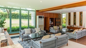 Un salón amplio con un gran ventanal que da a un jardín, muebles de mimbre, una estantería empotrada y una chimenea moderna.