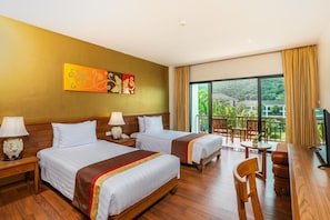 Quarto de hotel com duas camas, varanda com vista, piso de madeira e um quadro na parede.