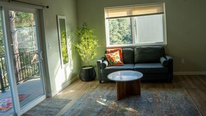 Een woonkamer met een bank, een bijzettafeltje, een potplant en uitzicht op het buitengebied door een raam.