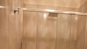 Cabina de ducha con mampara de vidrio, inodoro y lavamanos.
