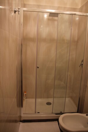 Cabina de ducha con mampara de vidrio, inodoro y lavamanos.