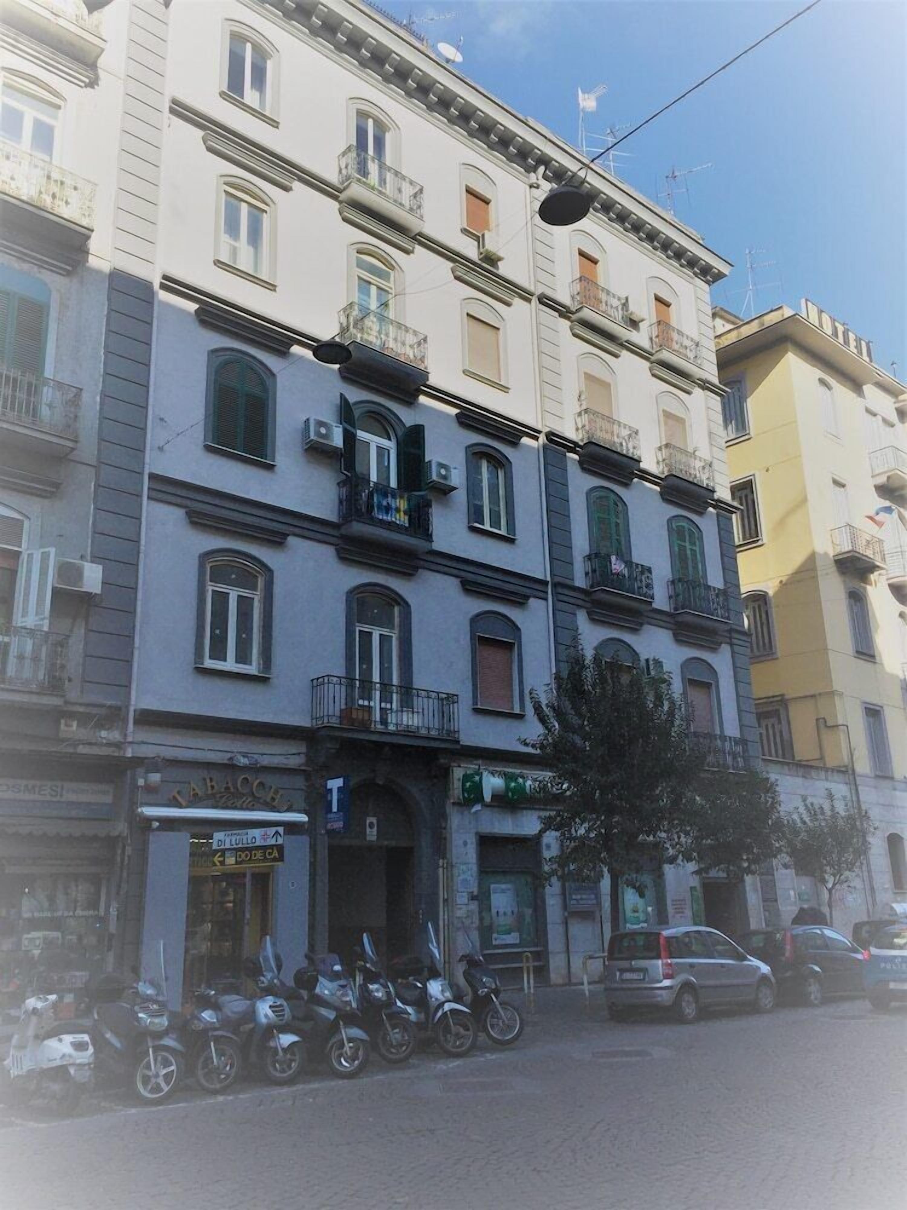 Un edifici de diversos pisos amb balcons, una botiga visible amb cartelleria i patinets aparcats.