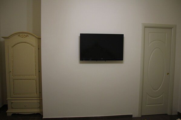 Una habitación con una televisión de pantalla plana montada en la pared, una puerta blanca y un armario de madera.