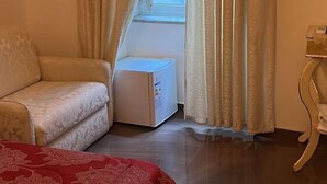 Un dormitorio con cama, sofá, radiador y ventana con cortinas.