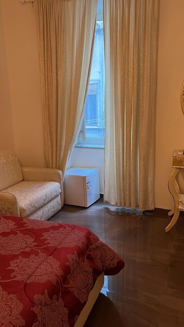 Un dormitori amb un llit, un sofà, un radiador i una finestra amb cortines.