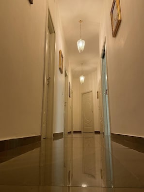Un pasillo con piso pulido, puertas y candelabros de cristal colgantes.