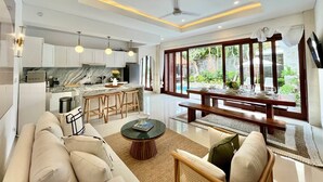 Una sala de estar moderna con sofá, mesa de centro y comedor con mesa preparada para cuatro personas.