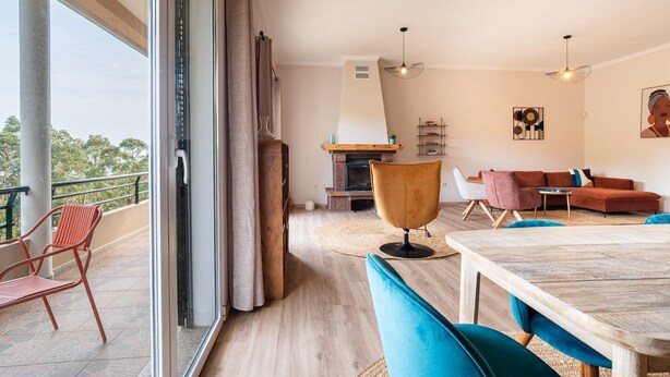 A spacious living area with a large window, a fireplace, a dining table, and a sofa. - GuestReady - Nature and tranquillity in Madeira (Gaula)