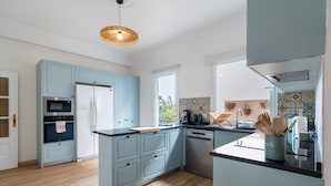 A modern kitchen with light blue cabinets, a central island, a built-in oven, and a dishwasher. - GuestReady - Nature and tranquillity in Madeira (Gaula)