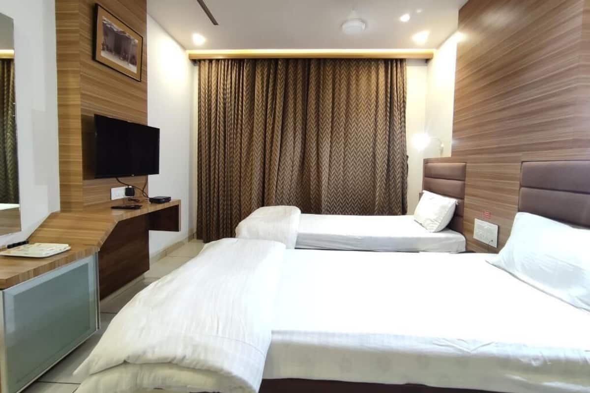 A hotel room with two beds, a desk, a flat-screen TV, and a large window with curtains.