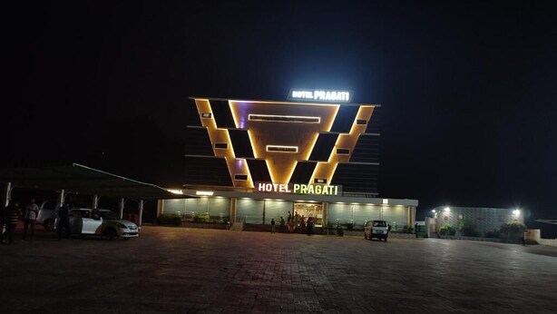 Un hotel con un llamativo letrero que dice 'HOTEL PRABATI', un área de entrada pavimentada y varios vehículos estacionados afuera.