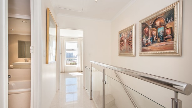 A hallway with a glass railing, a view of a bathroom, and two framed paintings on the wall. - 3 Canterbury Square (Cape Town)